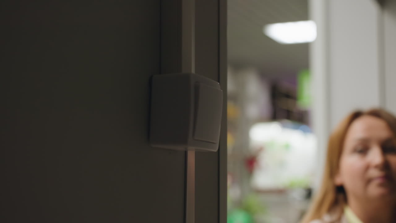 Dark service room with closed shutter as shop owner opens entrance and turns on light, faint outlines of switch and shutter visible, beginning of daily routine in business facility