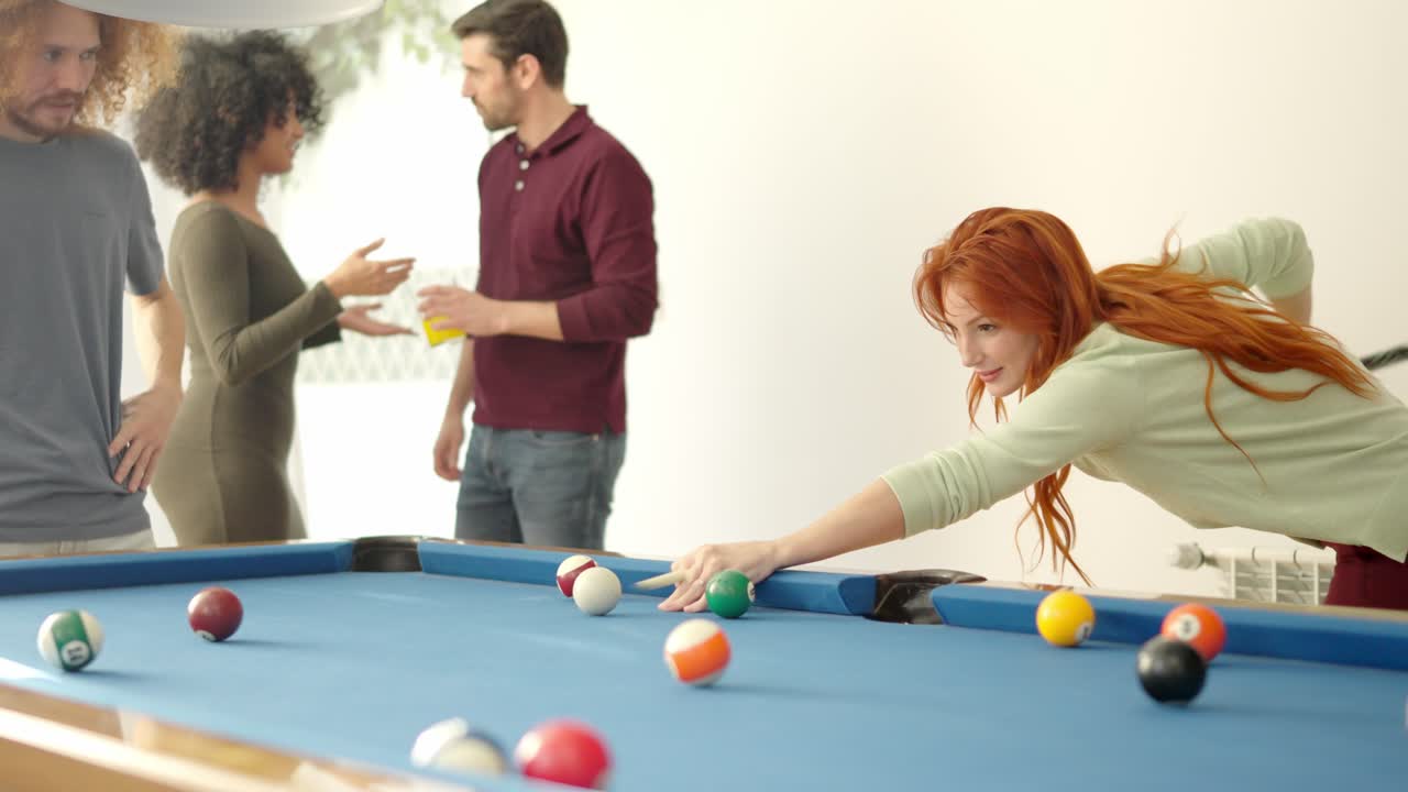 Woman hitting a ball playing pool with friends at home