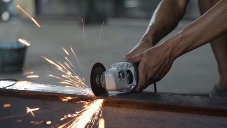 los trabajadores están cortando hierro usando un molinillo de mano, las chispas del molinillo están salpicando por todas partes
