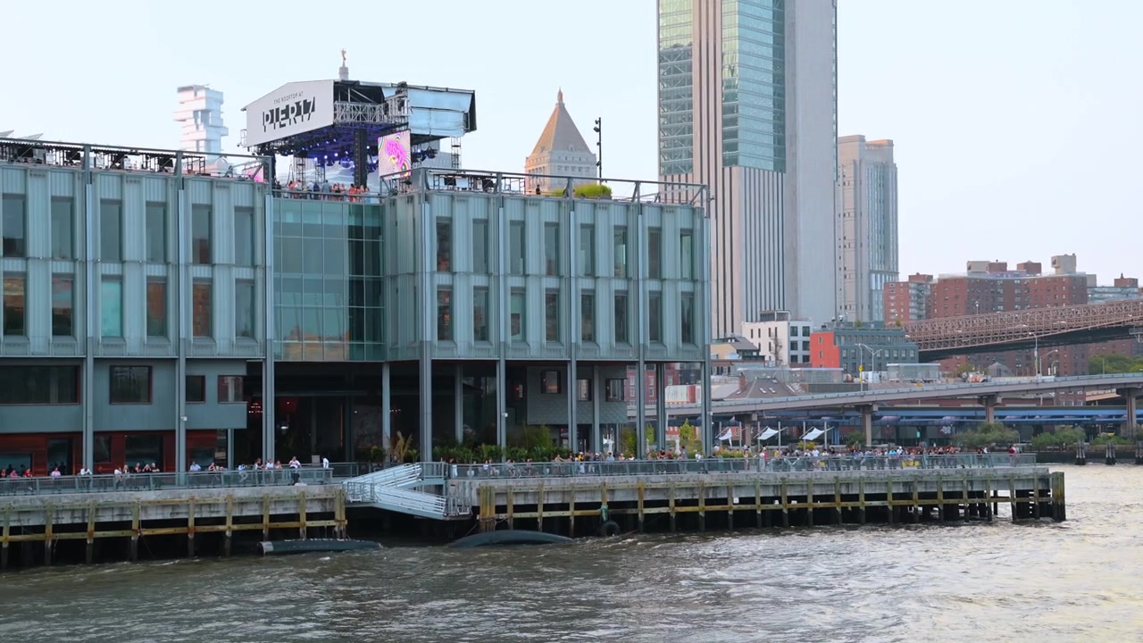 New York, Hoa Kỳ, 22 tháng 5 năm 2026: Sân thượng và gian hàng Pier 17 ở Hạ Manhattan, New York. Gian hàng kính hiện đại tại Pier 17 với mọi người trên lối đi lát ván trước đường chân trời Hạ Manhattan