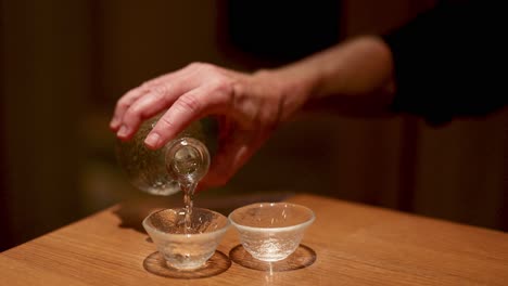 hands pouring clear liquid into small glass cups