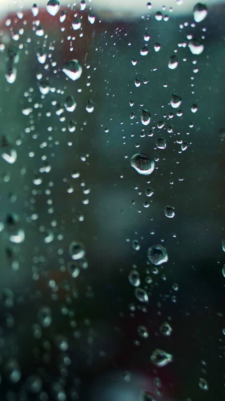 Bad weather. Rain falling outside. Rain on the glass. Rain drops on glass window. Water drops moving down on glass. Vertical video