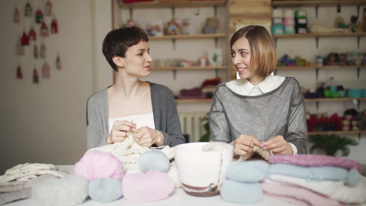 Donna che lavora a maglia sorride e parla con un'amica seduta al tavolo in un laboratorio.