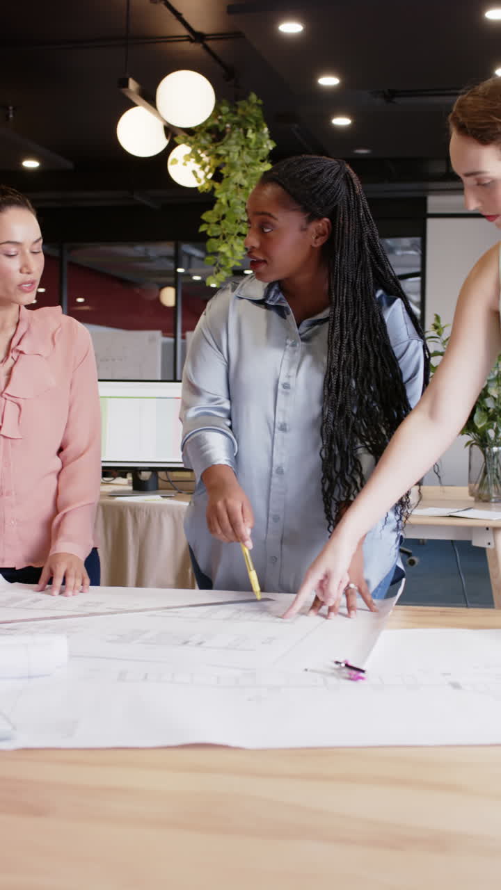 Vertical video of happy diverse businesswomen discussing architectural plans in office, slow motion