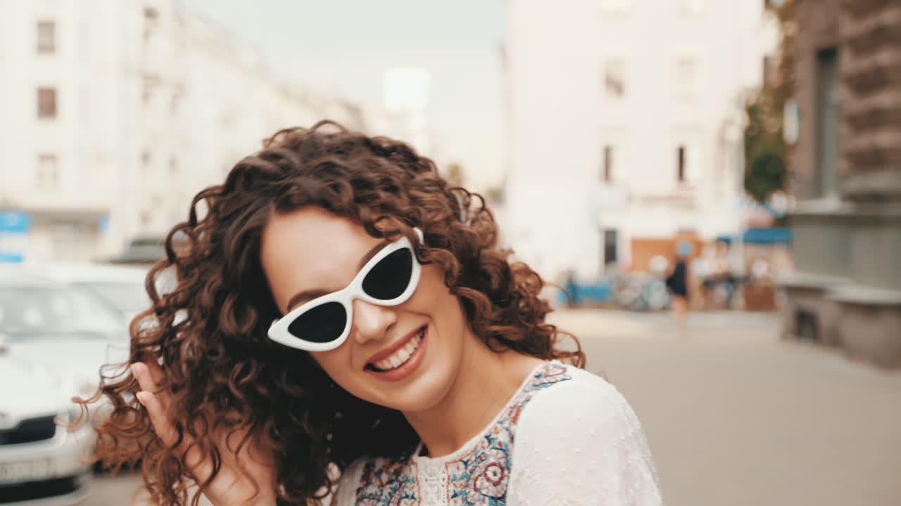 Young woman with curly hair and white sunglasses on city street