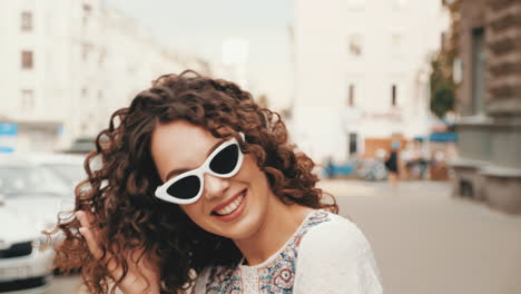 young woman with curly hair and white sunglasses on city street