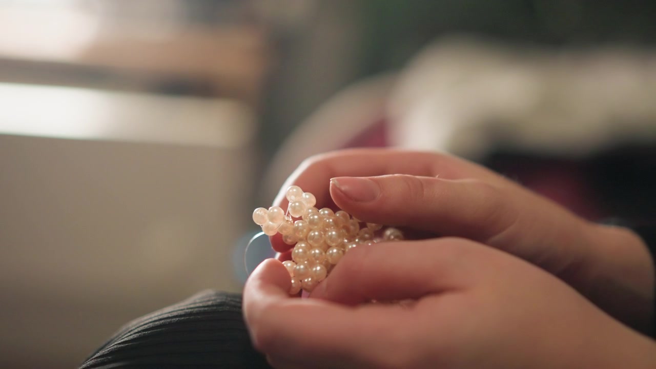 Vista ravvicinata dell'assemblaggio di delicati gioielli di perle. Ripresa dettagliata di mani esperte che creano un pezzo di collana di perle. Rappresentazione intima di un meticoloso lavoro manuale in un tranquillo laboratorio di gioielleria.