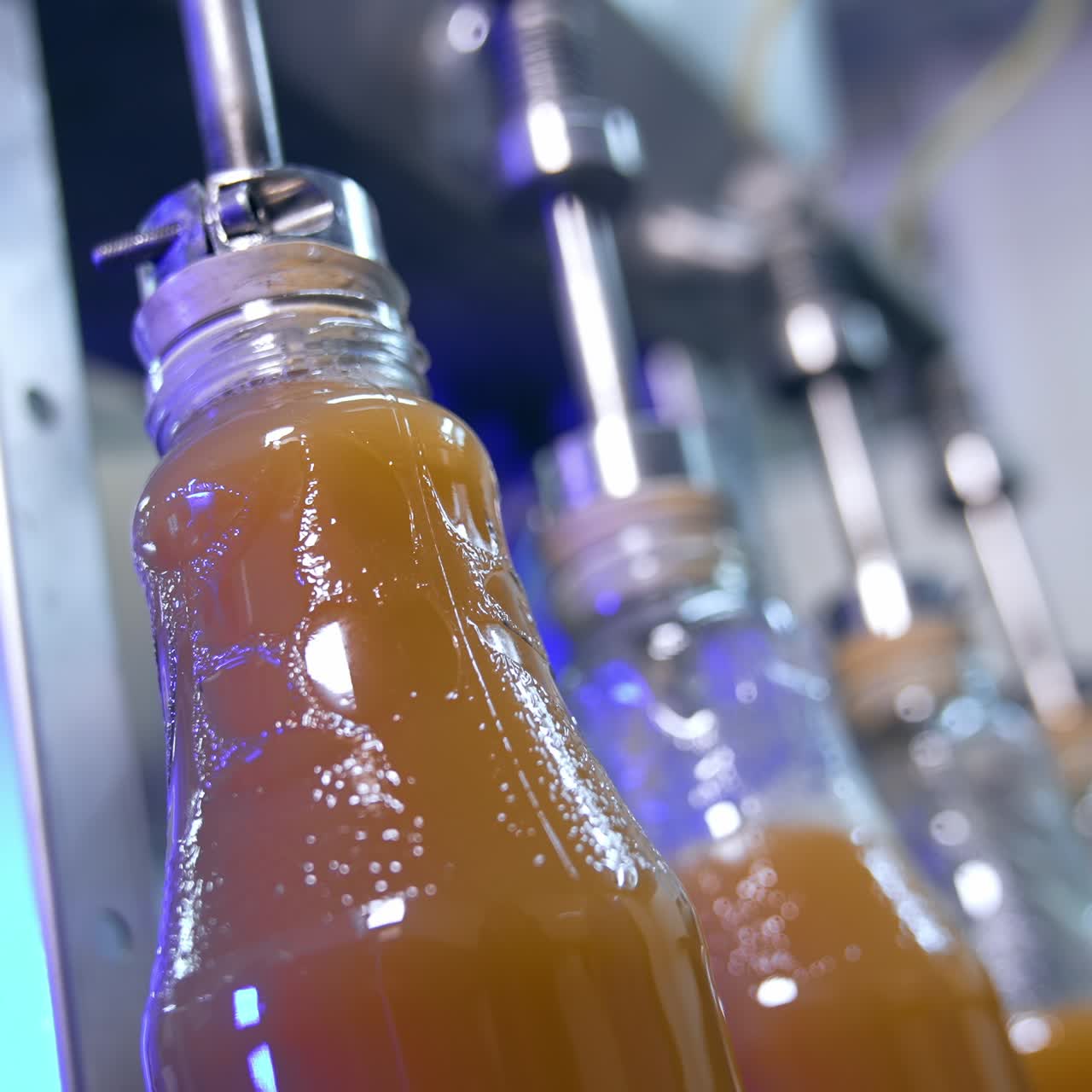 Few glass bottles being filled full with freshly-made juice. Automated technological process of juice manufacturing. Close up