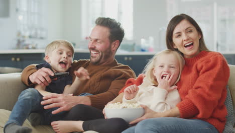 Familie-Sitzt-Mit-Popcorn-Auf-Dem-Sofa-Und-Schaut-Sich-Gemeinsam-Comedy-Im-Fernsehen-An