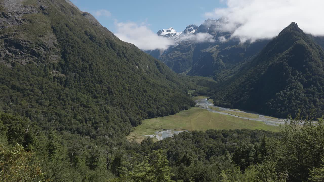 Views of the Routeburn river in a valley in between mountains and forest on a sunny summer day at Routeburn Track, New Zealand.