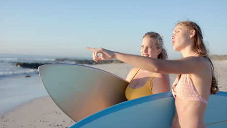 Two-young-Caucasian-women-stand-on-a-sunny-beach,-with-copy-space