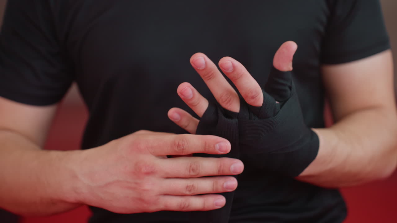 Boxer wraps fingers and hands with black bandages inside gym, focusing on protection, discipline, and preparation before training session, ensuring wrists and knuckles are secured for endurance, combat