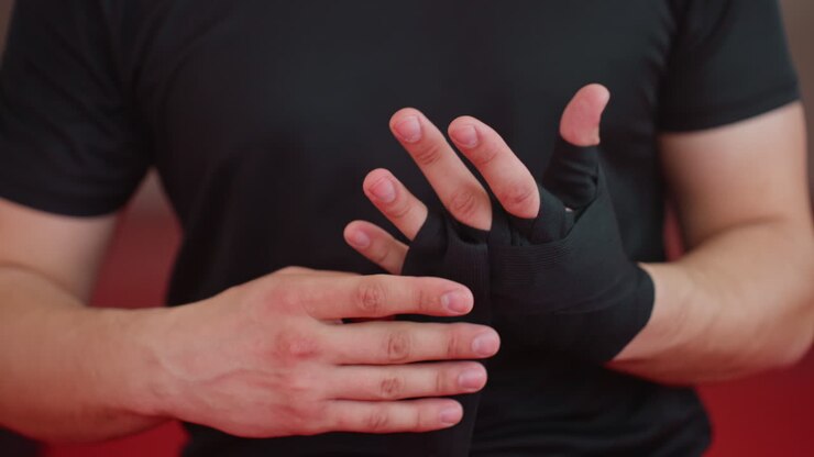 Boxer wraps fingers and hands with black bandages inside gym, focusing on protection, discipline, and preparation before training session, ensuring wrists and knuckles are secured for endurance, combat