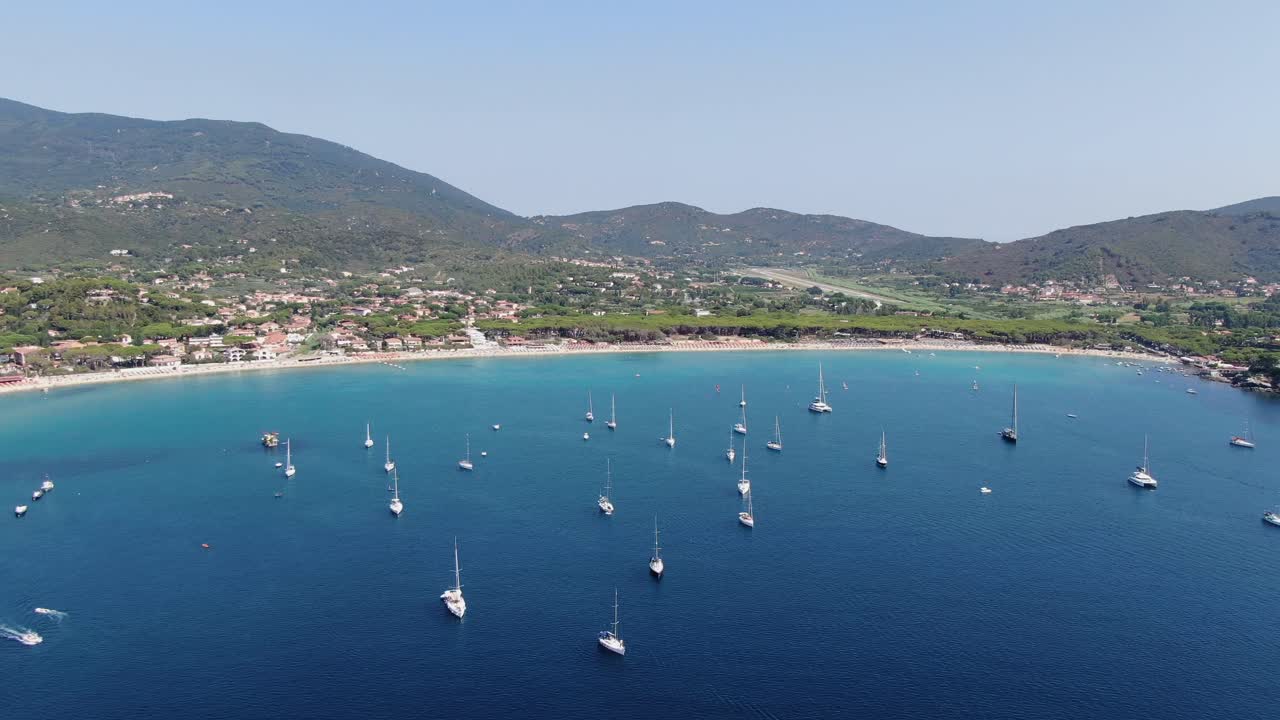 Vibrant beach atmosphere with people sunbathing, swimming, and boats floating in sparkling Mediterranean waters
