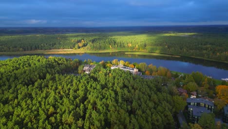 autumn forest in sunlight with dark clouds next to river in tradition lithuanian village