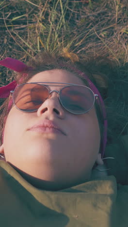 calm plus size young woman in sunglasses lies on dry grass at campsite in autumn evening close view