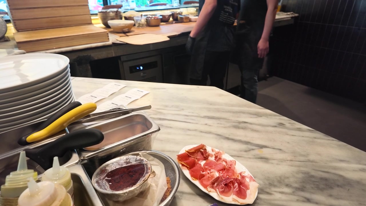 Primo piano di prosciutto affettato su un bancone di marmo con chef che lavorano sullo sfondo