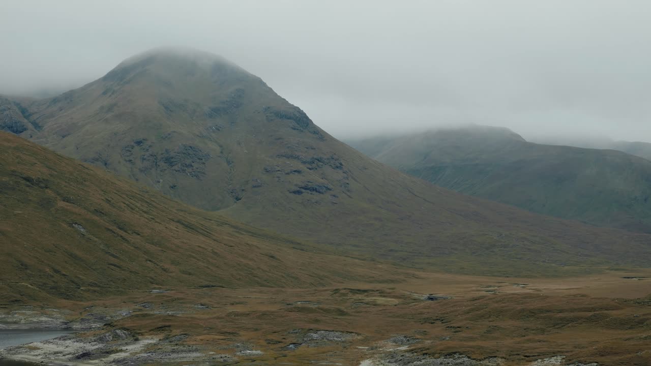 Inquadratura di apertura delle Highlands scozzesi, Scozia, con ampie vedute collinari e paesaggi montani aspri, valli verdi aperte sotto nuvole nebbiose.