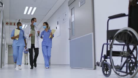 diverse group of male and female doctors wearing face masks walking in hospital corridor talking