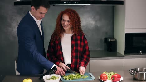 the man in business, elegant suit returns home from work where he is waited by the careful beautiful wife and prepares a dinner. handsome husband kisses and hugs his woman. loft interior kitchen