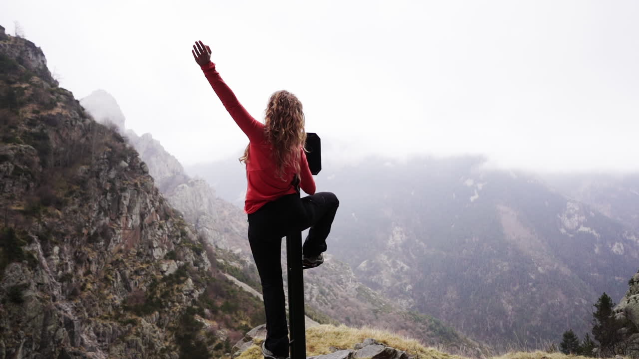 cámara lenta de una exitosa joven rubia fitness liberando su felicidad después de llegar a la cima de las montañas en una larga aventura al aire libre