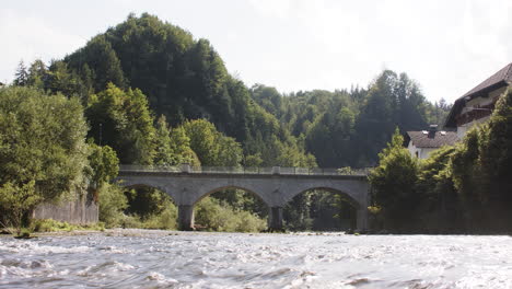 Histórico-Puente-De-Piedra-Sobre-Un-Pintoresco-Río-Bajo-El-Sol,-Paisaje-De-Montaña