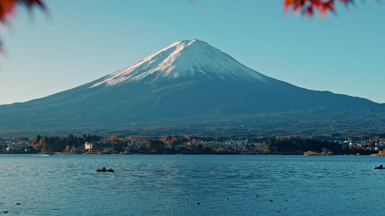 Una splendida inquadratura inclinata che cattura il maestoso Monte Fuji incorniciato da vivaci foglie autunnali rosse lungo le rive del Lago Kawaguchiko.