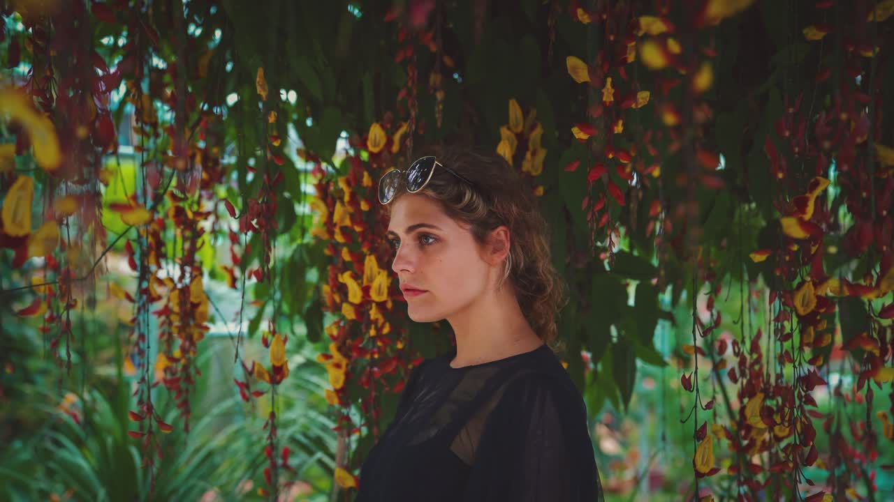 4k uhd cinemagraph молодой женщины брюнетки, стоящей рядом с красивым красочным деревом с множеством цветков, движущихся вокруг ее головы