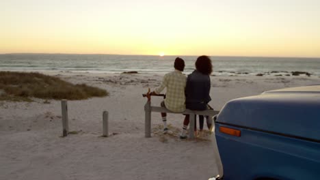 Vista-Trasera-De-Una-Pareja-Afroamericana-Sentados-Juntos-En-Un-Bolardo-En-La-Playa-4k