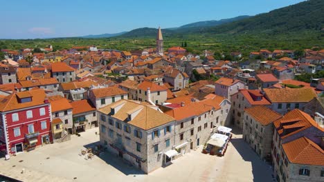 panorama of a coastal town with many houses with red roofs, surrounded by the sea and mountains with yachts in marina bay and bell tower and people on bike