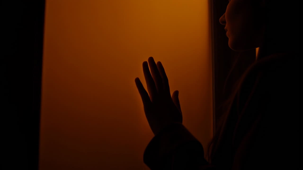 Silhouette of a person touching a wall in dim light
