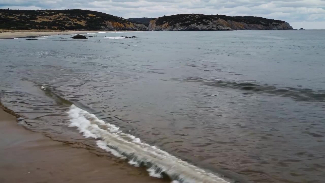 Onde leggere che si infrangono su una spiaggia sabbiosa in una giornata nuvolosa