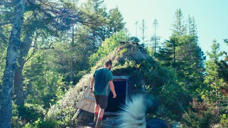 un hombre con un perro entrando en el refugio de bushcraft casa en el bosque con puerta de madera