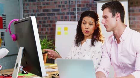 Businesswoman-interacting-with-coworker-while-working-on-computer