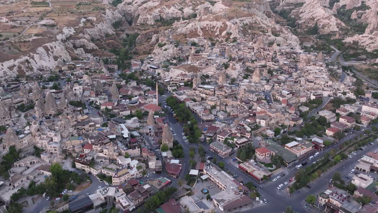 Panoramic aerial overview of Cappadocia’s valleys and rocky terrain at sunrise, showcasing the unique formations of the landscape merging with the urban environment