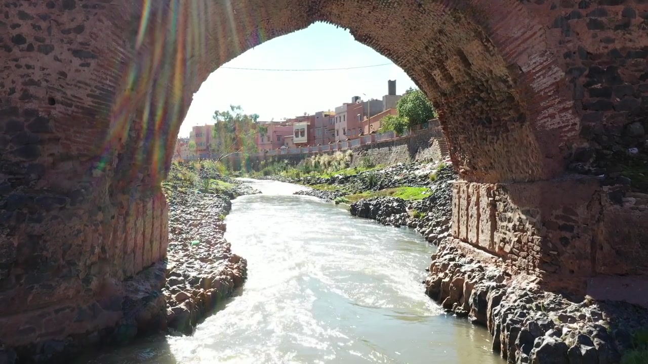 Puente de piedra iluminado por el sol cruzando un río caudaloso en un pueblo marroquí con reflejos naturales y un paisaje tranquilo. Paisaje cinematográfico ideal para proyectos de viajes, cultura y documentales