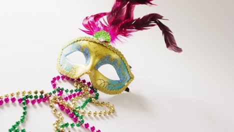 video of masquerade mask with pink feathers and mardi gras beads on white background with copy space