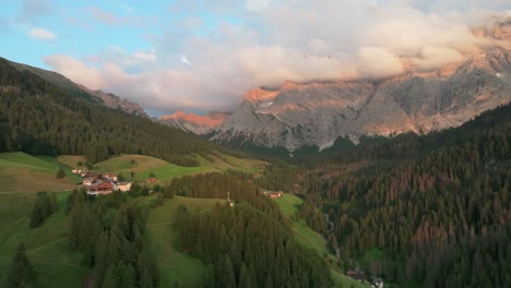 Eine-Abendliche-Luftaufnahme-Von-Abgelegenen-Häusern-Des-Dorfes-La-Val-Mit-Dem-Majestätischen-Berg-Sas-Dles-Nü,-Der-Im-Hintergrund-Von-Wunderschönen-Wolken-Bedeckt-Ist