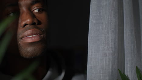 unhappy and depressed young man at home opening curtains and looking out of window 2