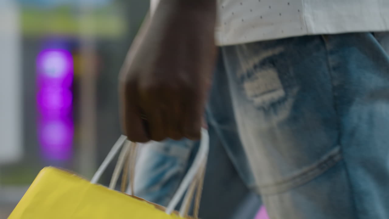 Side view of person in casual outfit holding shopping bag while walking through brightly lit retail space, denim jeans visible with background blur