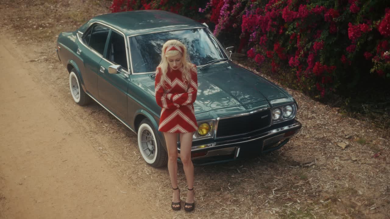 Donna elegante che posa con auto d'epoca su una strada sterrata