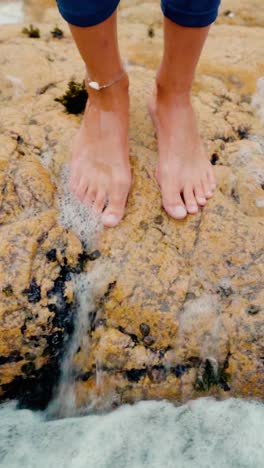 feet standing on ocean rocks as waves wash over