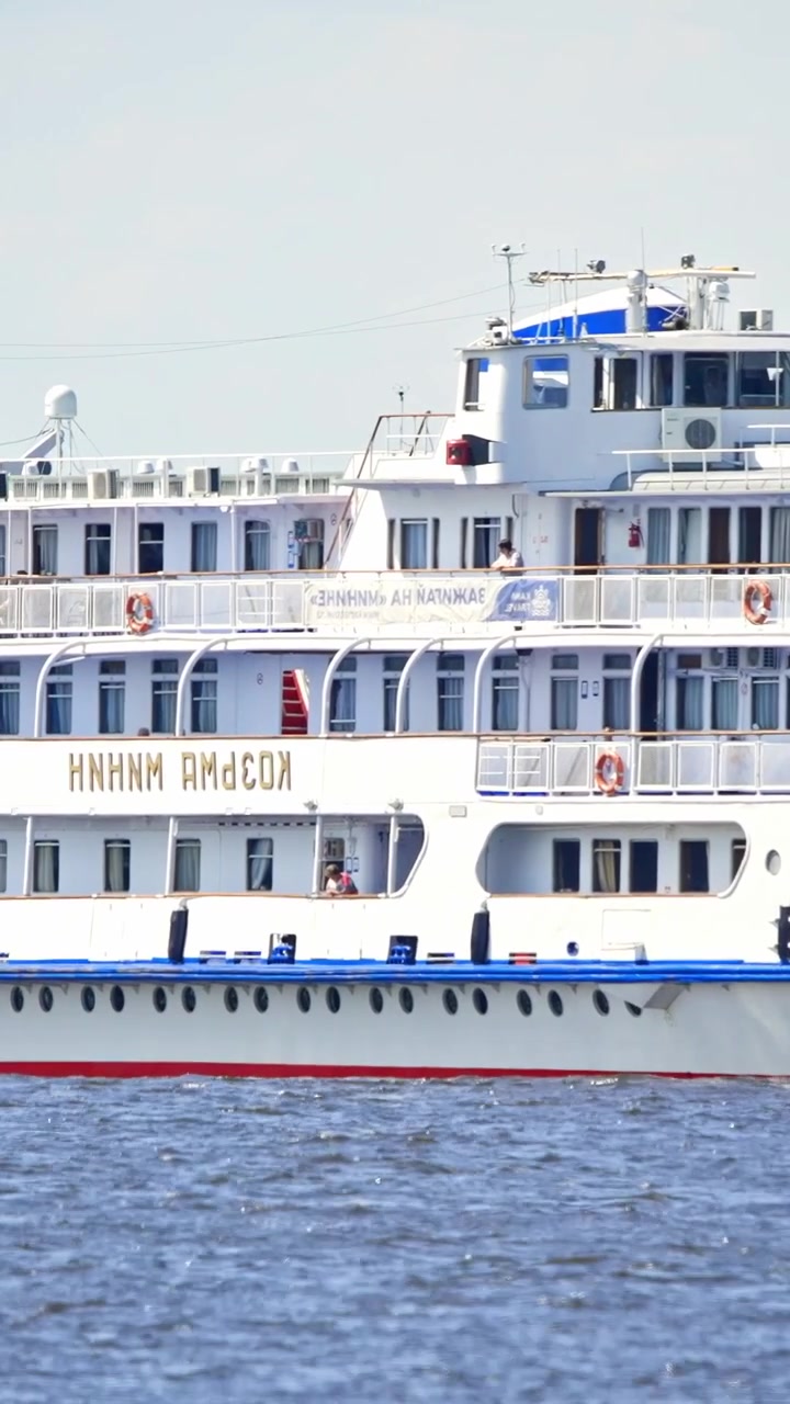 Stort hvidt flodkrydstogtskib navigerer på en bred flod på en solrig dag