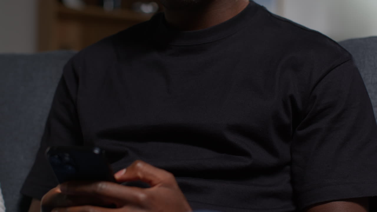 Close Up Of Unhappy And Depressed Young Man Sitting On Sofa At Home Messaging Or Browsing On Mobile Phone