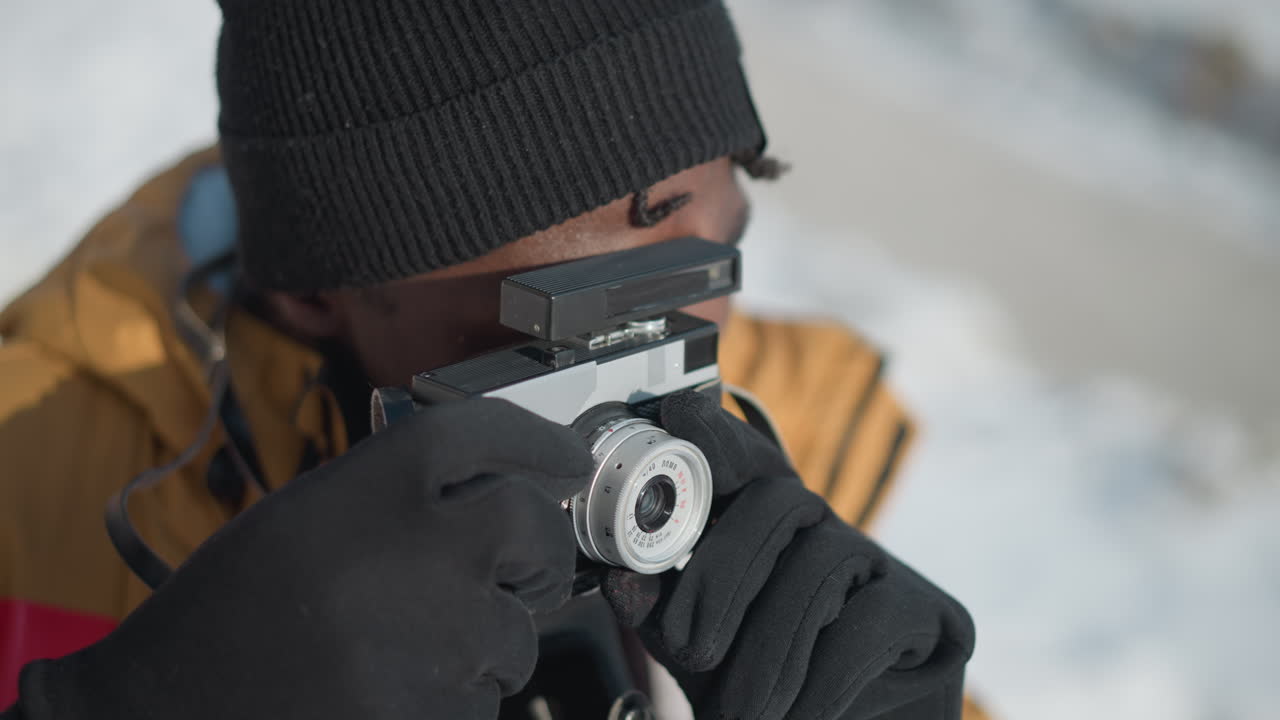 high angle view of professional photographer peering through viewfinder of vintage camera, gloved hand adjusting lens dial and pressing shutter for precise focus under bright winter sunshine