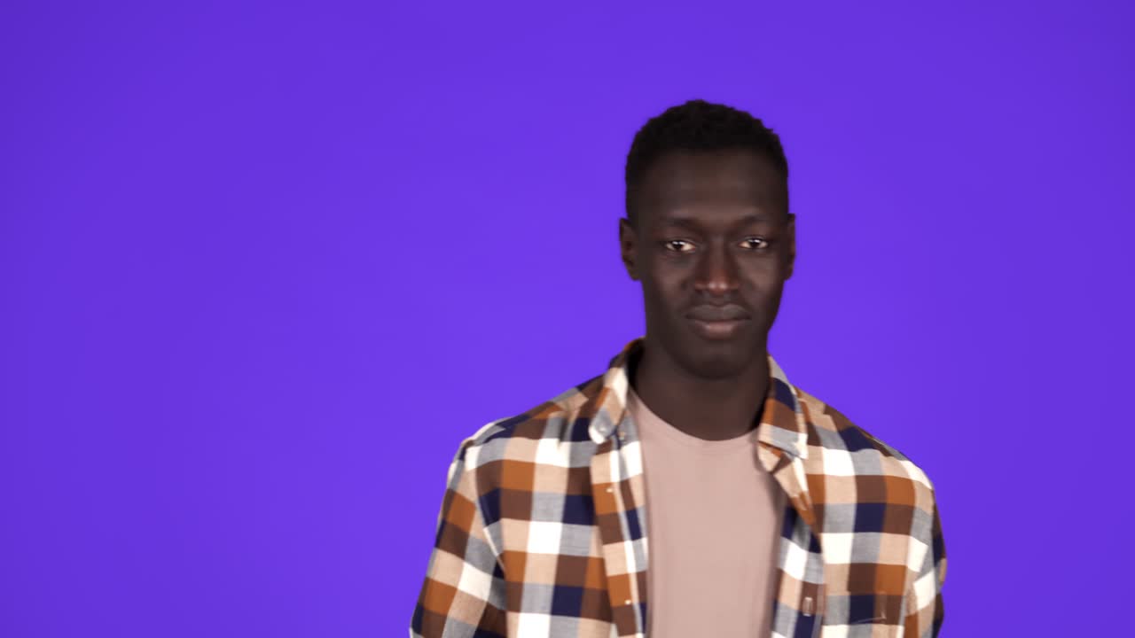Happy, smiling african american man in good mood on blue background. Gesturing with thumbs up, like gesture, touching his plaid shirt - human emotions
