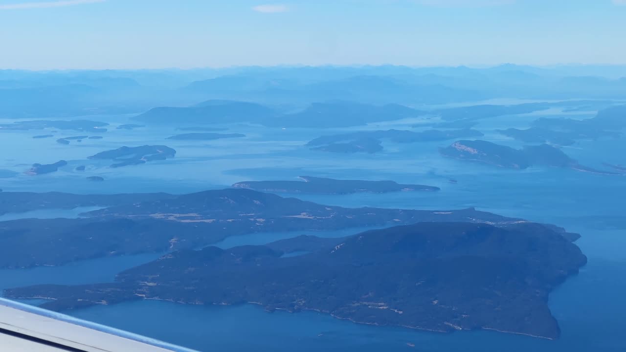 Airplane window POV shot of Vancouver Island in the distance while flying over the Salish Sea between the United States and Canada. 4K
