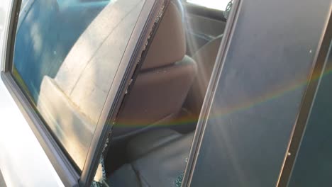 Rear-car-window-glass-smashed-and-broken-from-attempted-vehicle-theft-and-robbery,-shattered-glass-scattered-on-back-car-seats