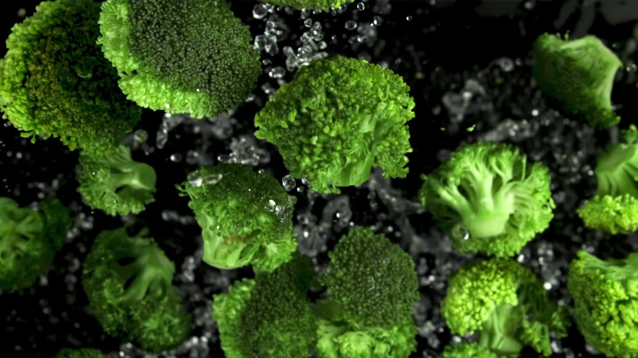 Cimette di broccoli fresche che schizzano nell'acqua su sfondo nero al rallentatore.