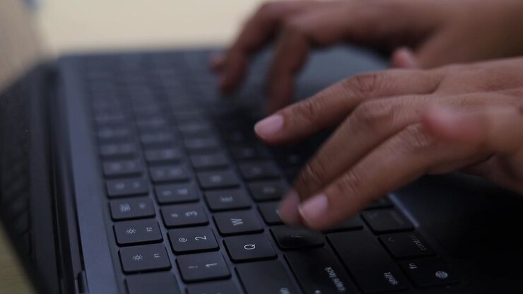 Primo piano delle mani di una persona che digita rapidamente su una tastiera scura di un computer o laptop, rappresentando la digitazione, il lavoro, la produttività in ufficio, la tecnologia digitale e la comunicazione online